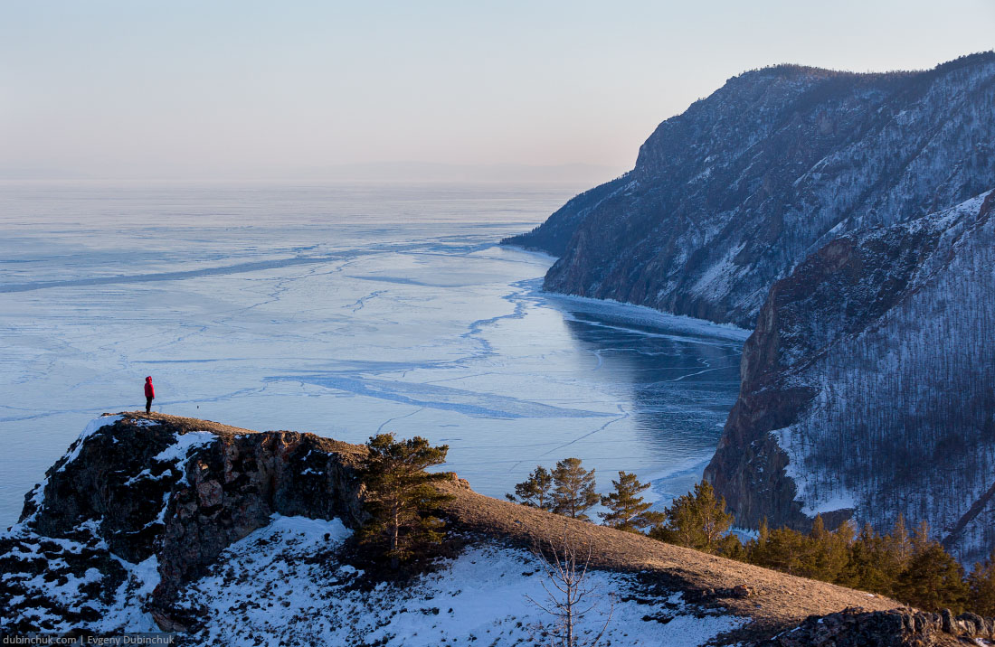 Путешественник на краю обрыва на озере Байкал зимой. Вид на замерзший лед с высоты птичьего полета