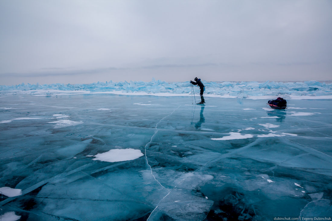 Путешествие на коньках по Байкалу зимой. Девушка на фоне синих торосов в пасмурную погоду