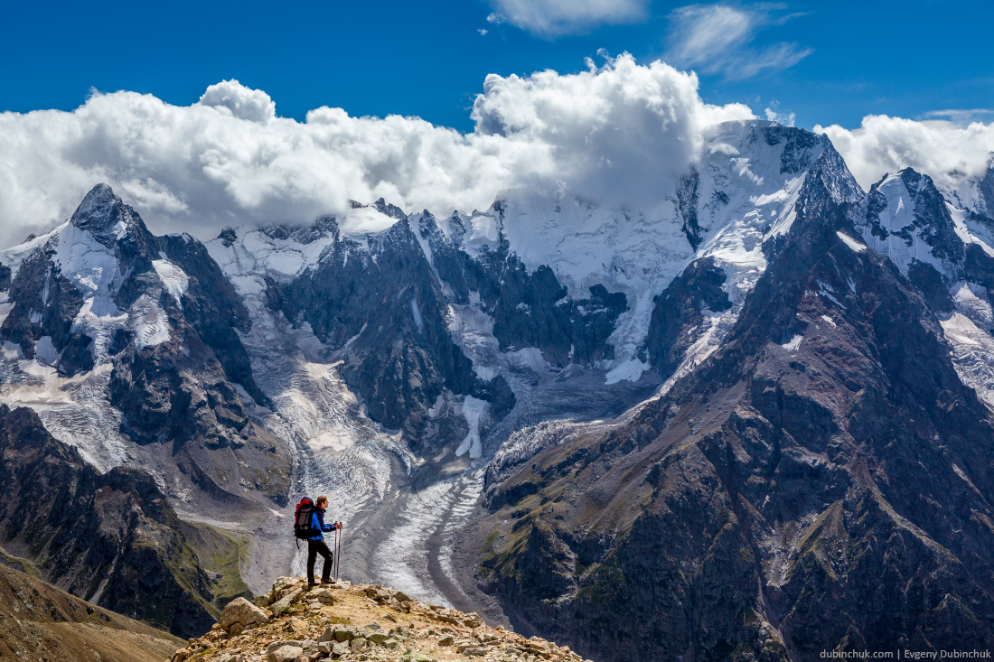 Hiker with backpack standing on mountain top and enjoying scene. Caucasus mountains, Russia